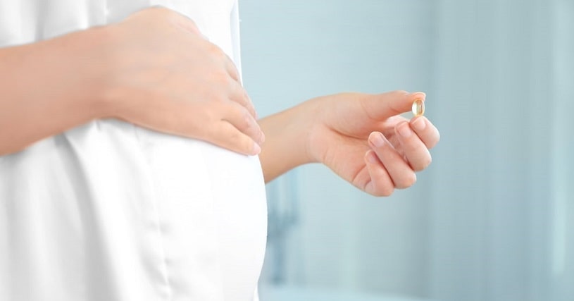 Pregnant woman holding a capsule pill.