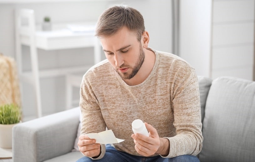 Man reading pill instructions on the couch at home.