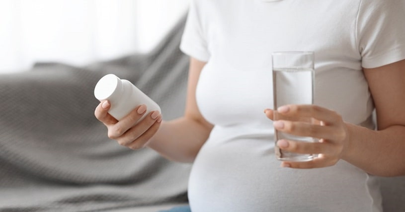Pregnant woman holding meloxicam and a glass of water.