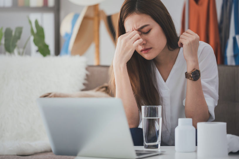 A woman in pain sits at the table with Vyvanse pills on it.