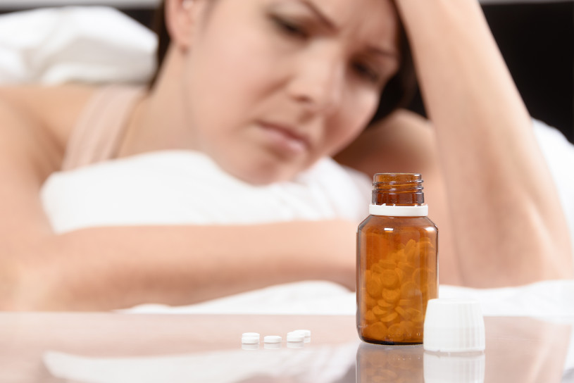 An upset woman looks at pills.
