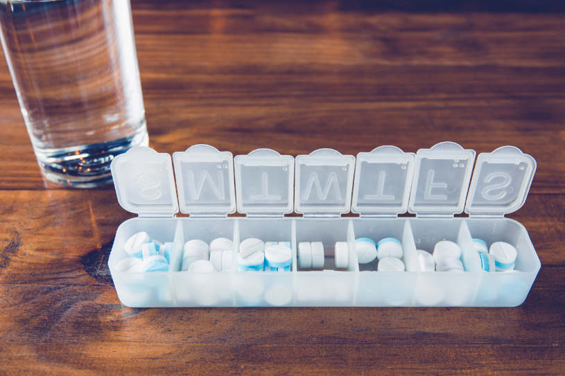 An organizer with Phenobarbital pills and a glass of water on the table.