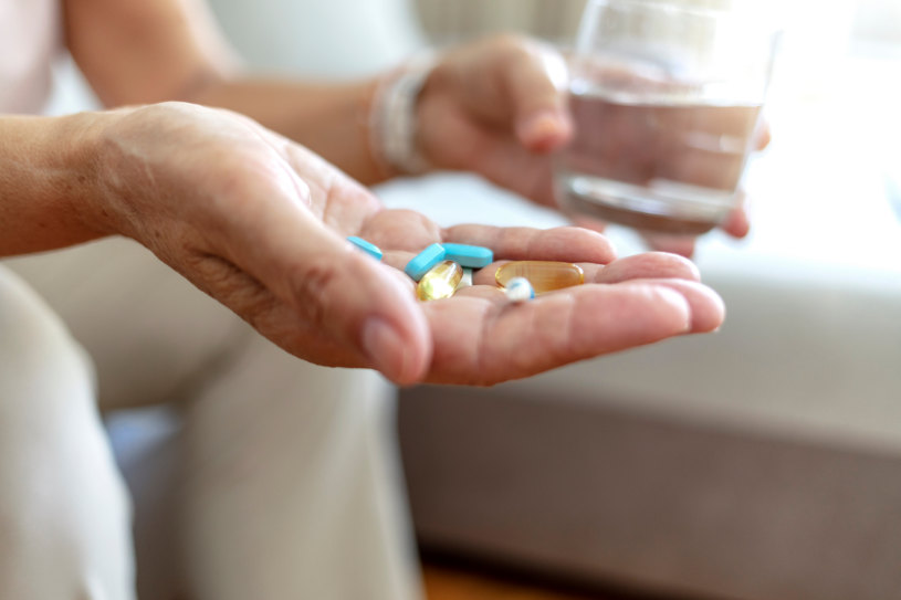 A man holds different pills and a glass of water.