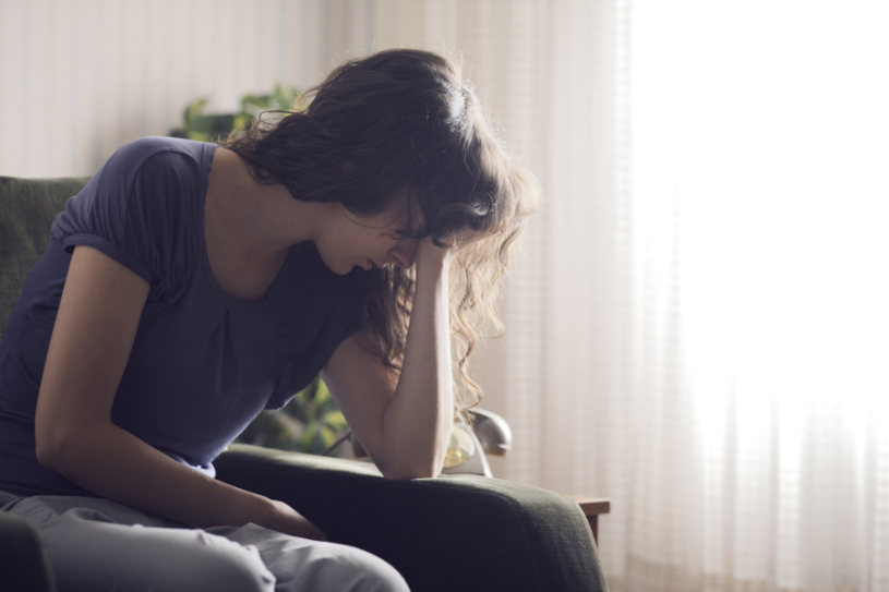 A woman experiencing Pristiq side effects sits on sofa.