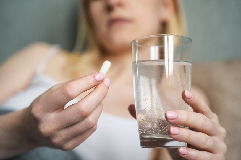 A woman holds Remeron pill and a glass of water.