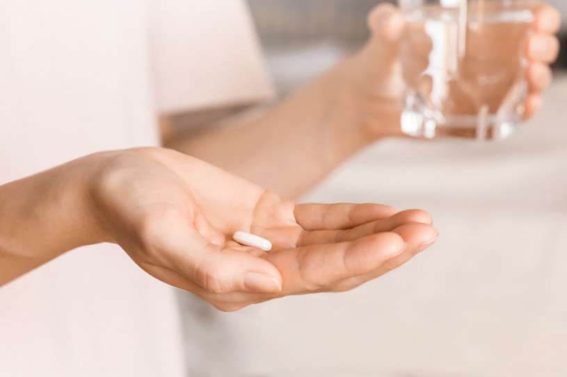 A woman holds Trazodone pill in one hand and a glass of water in the other.