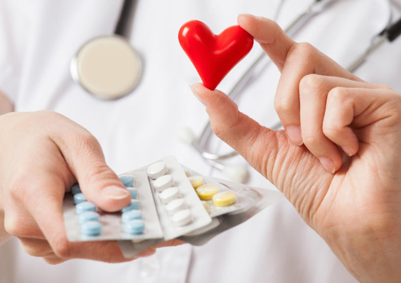 A doctor holds a plastic red heart and some pills in her hands.