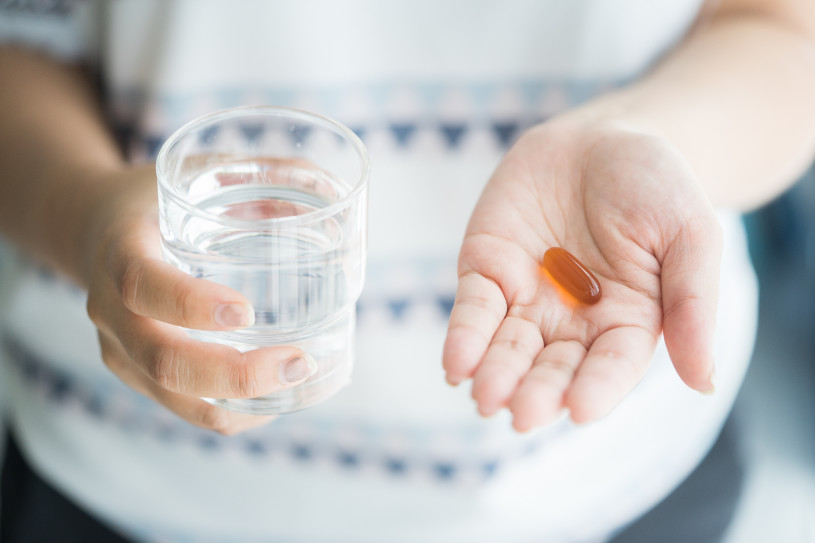 A woman holds a pill and a glass of water in her hands.