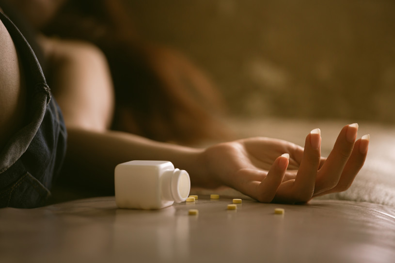 A woman lying in bed and pills dropзed near her hand.