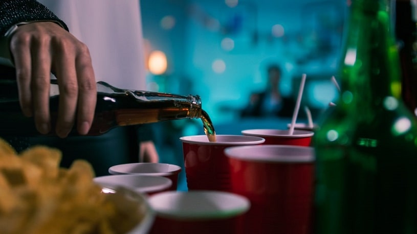 Person pouring drink from a bottle into a red cup.