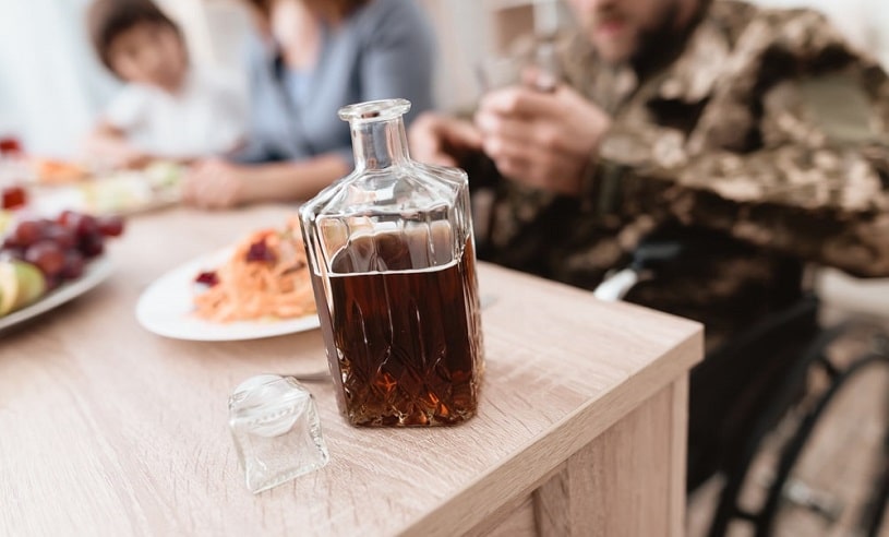 Veteran in a wheelchair and a bottle of whiskey on the table.