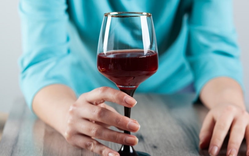 Woman addict holding a glass of red wine.