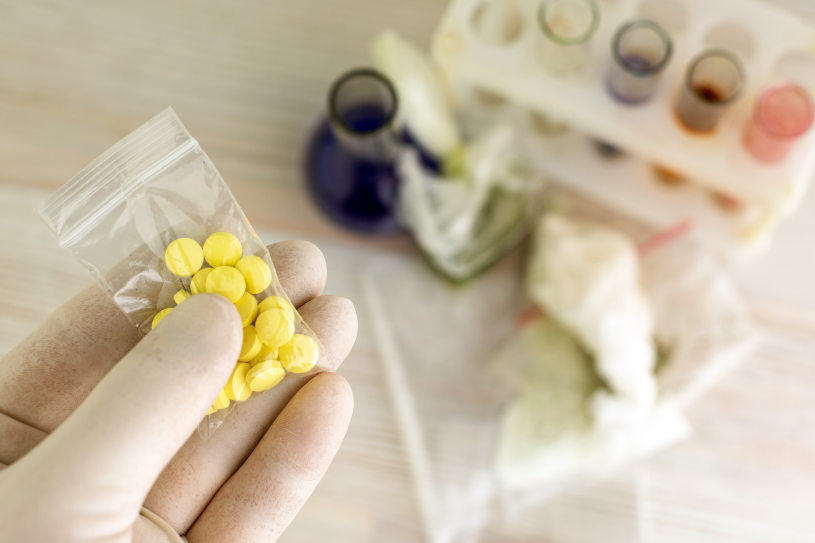 A person holds a small bag of yellow drugs and test tunes on the background.