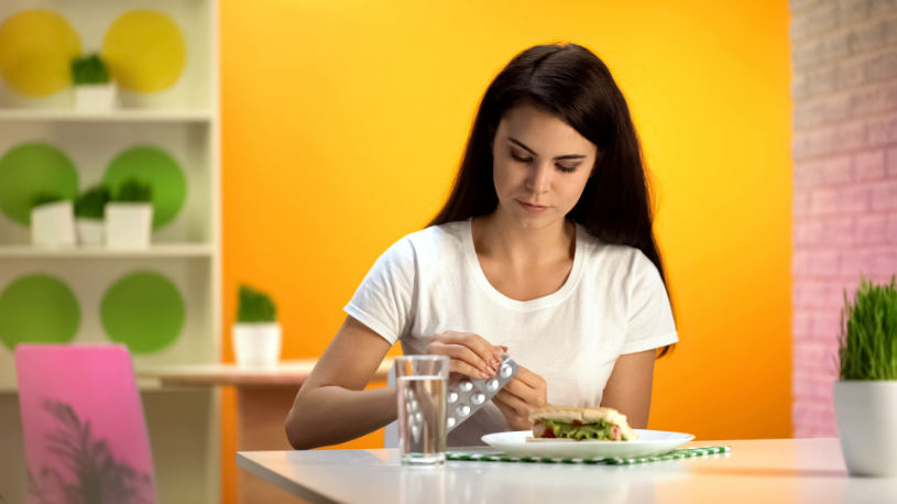 A woman with a sandwich on plate takes a paxil pill.