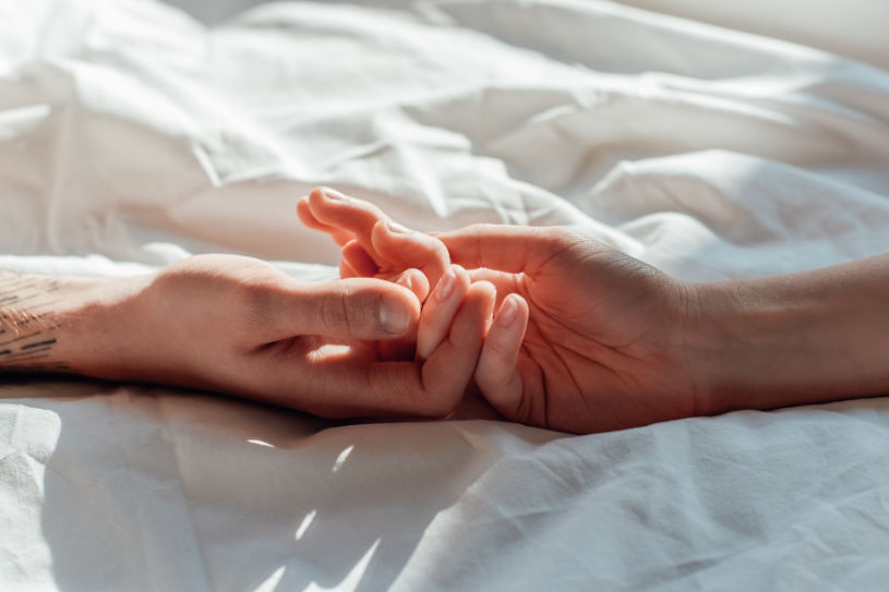 A woman's hand and a man's hand on bed.