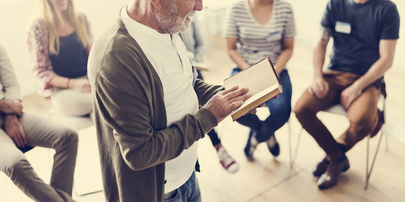 Senior male reads Alcoholics Anonymous Big Book.