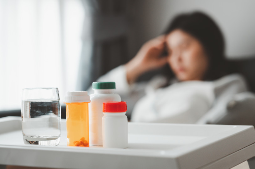 Buspar pills and a glass of water with a woman with a headache on the background.