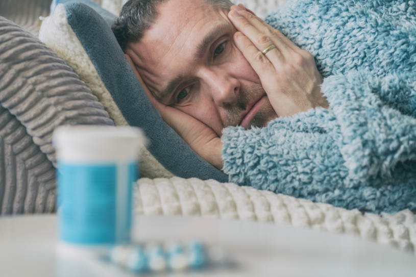 A depressed man looks at pills on the table.