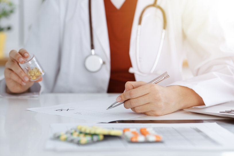 A doctor holding a bootle of pills and writing a prescription.