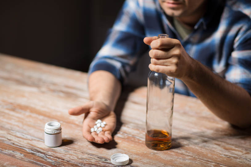 A man holds a bottle of alcohol and antidepressant pills in his hand.