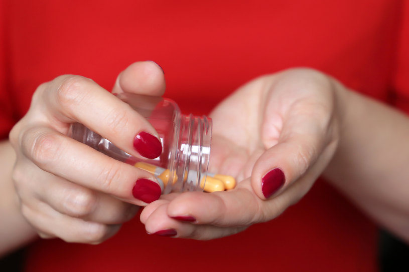 A woman in red pouring some pills in her hand.