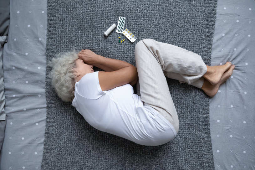 A woman lying in bed with some pills on the blanket.