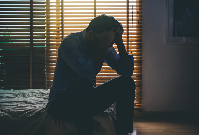 Depressed man sitting head in hands on the bed in the dark bedroom.